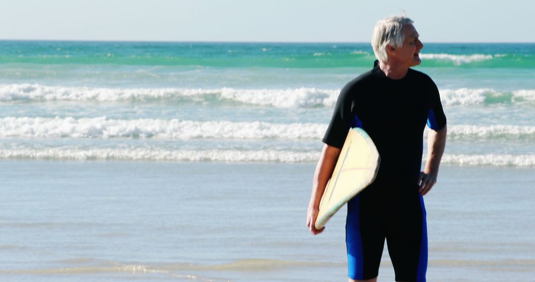 A middle-aged Caucasian man stands on a beach holding a surfboard, with copy space - Free Images, Stock Photos and Pictures on Pikwizard.com