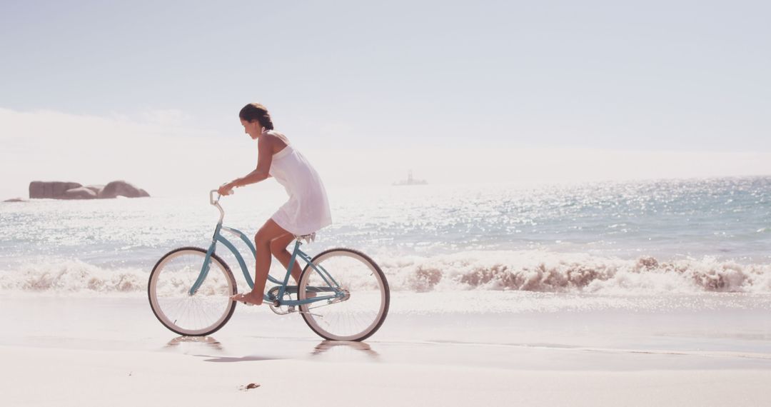 A woman in a white dress cycles peacefully on a beach, evoking a tranquil summer vibe. - Free Images, Stock Photos and Pictures on Pikwizard.com