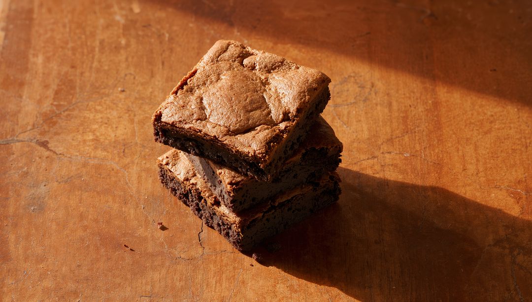 Sunlit Stack of Fudgy Chocolate Brownies on Rustic Wooden Tabletop with Crumbs and Shadow