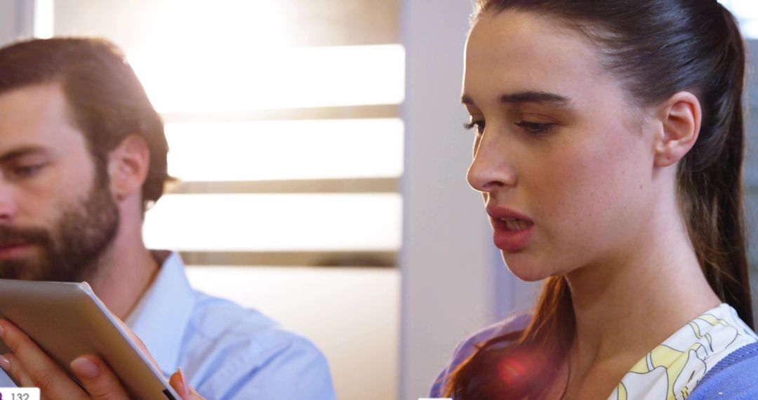 Female professional reviewing tablet report while colleague consulting digital device in modern work