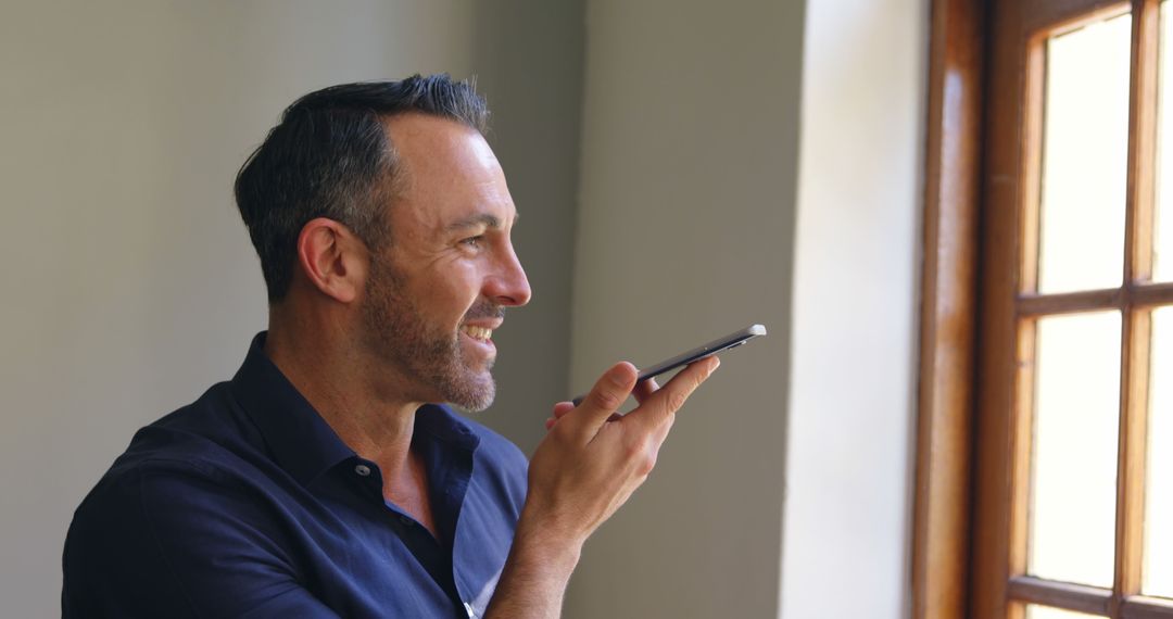 Happy Man Using Voice Command on Smartphone Near Window - Free Images, Stock Photos and Pictures on Pikwizard.com