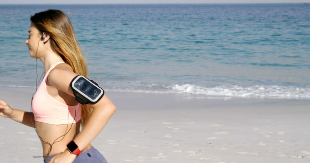 Young Woman Jogging on Beach with Earphones and Armband - Free Images, Stock Photos and Pictures on Pikwizard.com