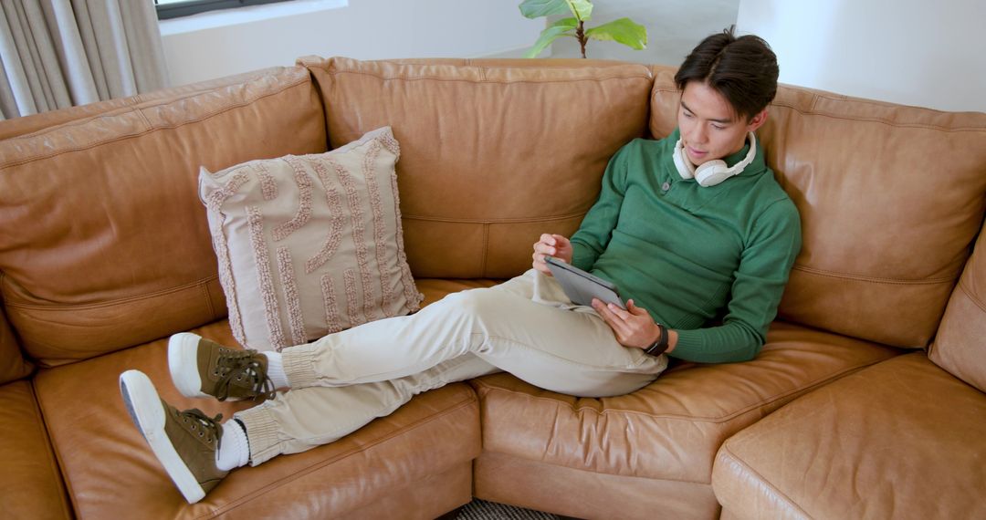 Asian Man Relaxing on Leather Sofa Using Tablet Technology