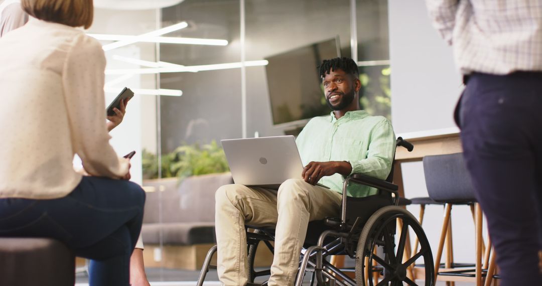 Inclusive Workplace Discussion with Man in Wheelchair Using Laptop