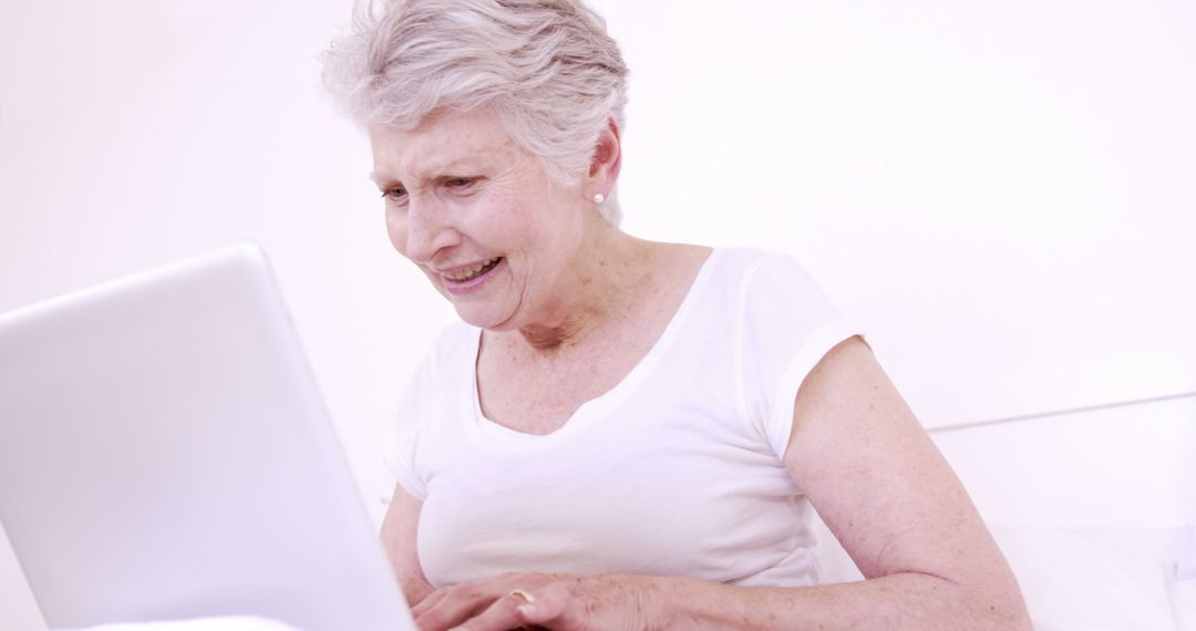 Senior Woman Using Laptop, Smiling and Engaged in White Room - Free Images, Stock Photos and Pictures on Pikwizard.com