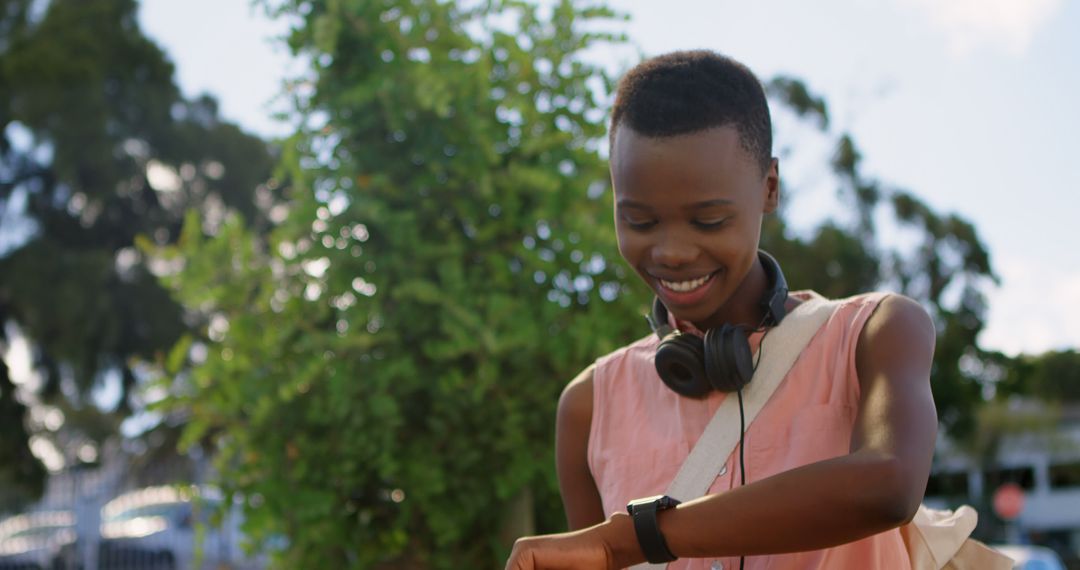 Happy Student with Headphones Checking Smartwatch Outdoors - Free Images, Stock Photos and Pictures on Pikwizard.com