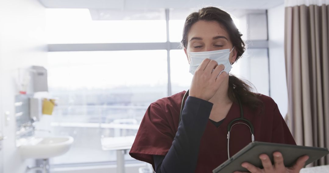 Tired Healthcare Worker Wearing Mask and Holding Tablet in Hospital - Free Images, Stock Photos and Pictures on Pikwizard.com