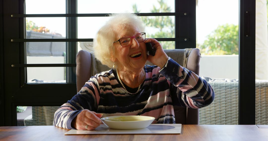 Happy Senior Woman Talking on Phone While Eating Soup - Free Images, Stock Photos and Pictures on Pikwizard.com