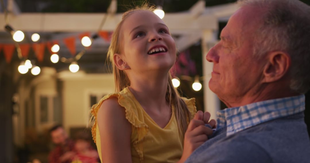 Grandfather Holding Granddaughter, String Lights in Background at Backyard Party - Free Images, Stock Photos and Pictures on Pikwizard.com