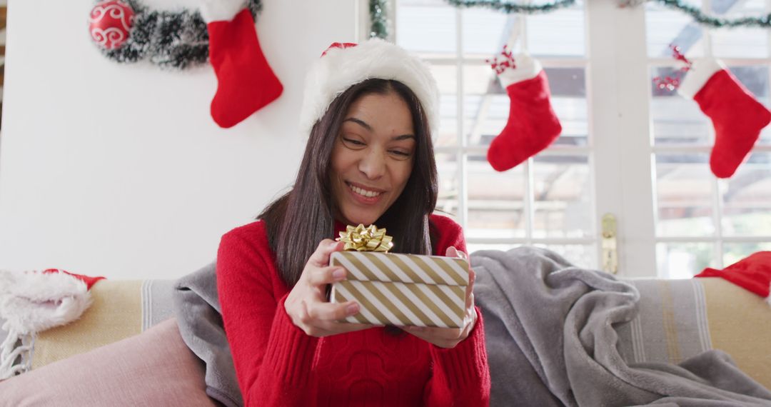 Smiling Woman Holding Christmas Gift on Festive Couch - Free Images, Stock Photos and Pictures on Pikwizard.com