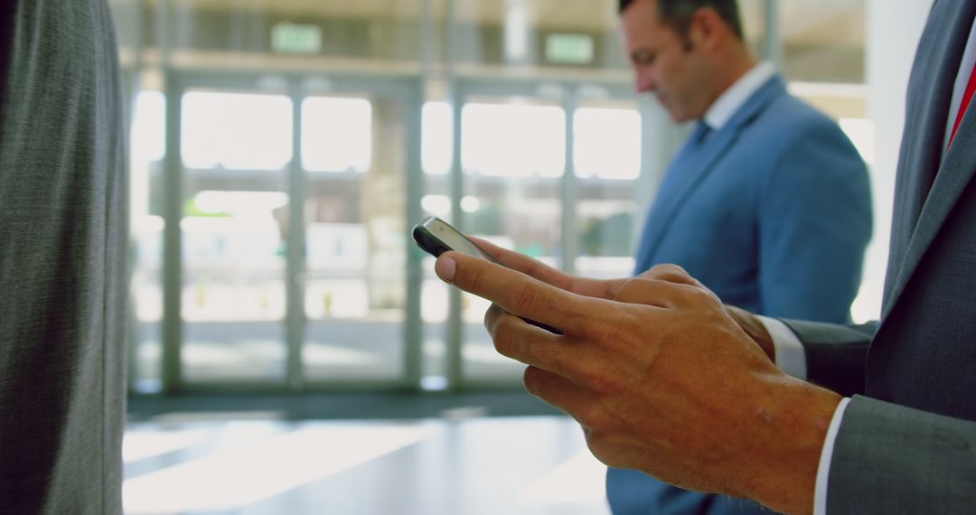 Businessman Checking Smartphone in Busy Office Lobby - Free Images, Stock Photos and Pictures on Pikwizard.com