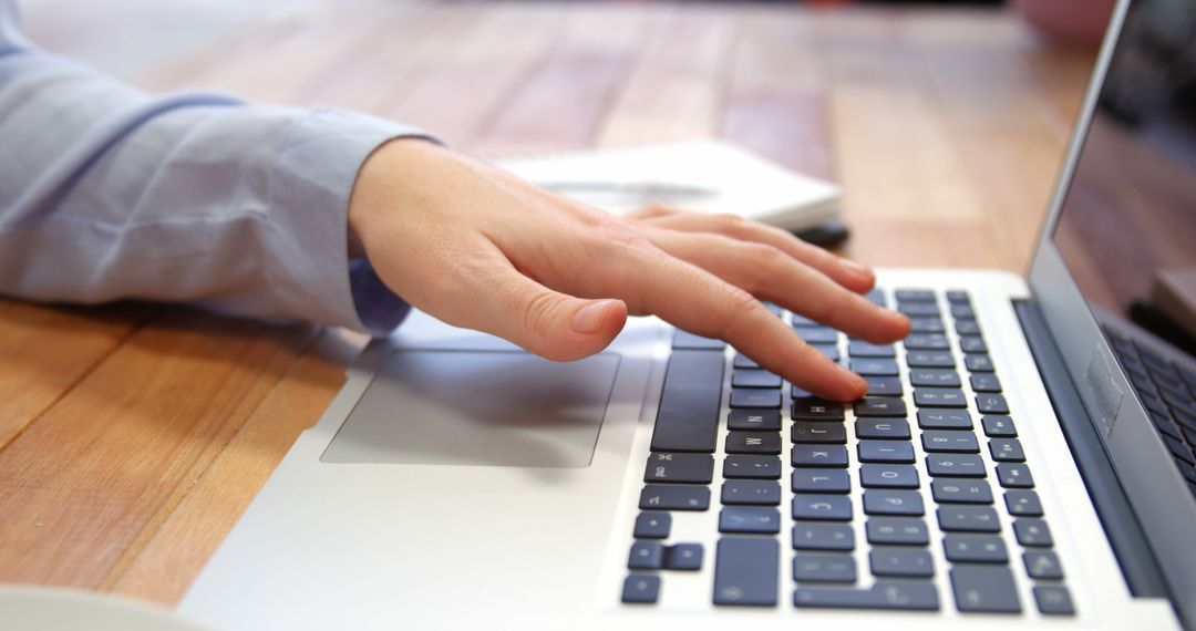 Working on Laptop with Hand on Keyboard on Wooden Desk
