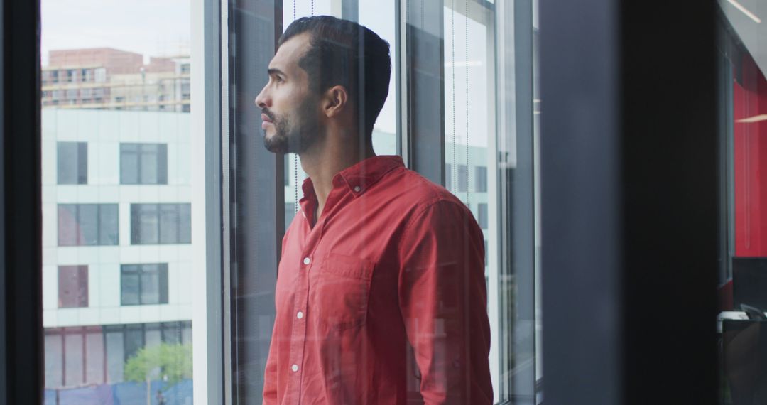 Contemplative Man in Red Shirt Gazing Out of Office Window - Free Images, Stock Photos and Pictures on Pikwizard.com