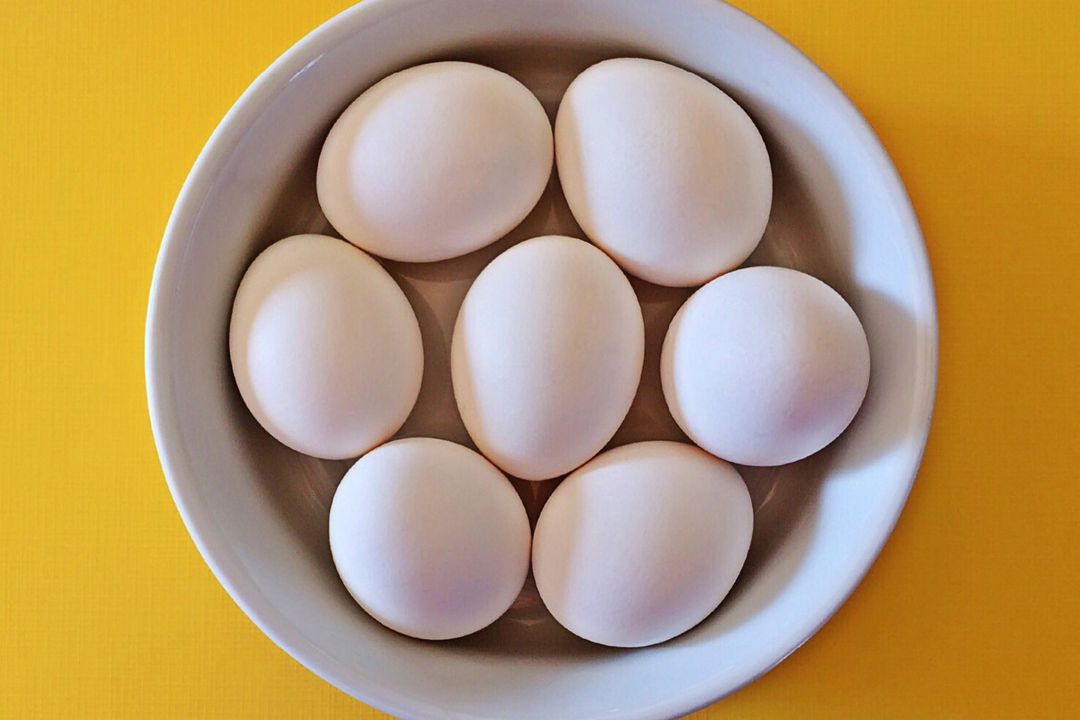 Top-down Arrangement of Seven White Eggs Nesting in Ceramic Bowl on Bright Yellow Surface