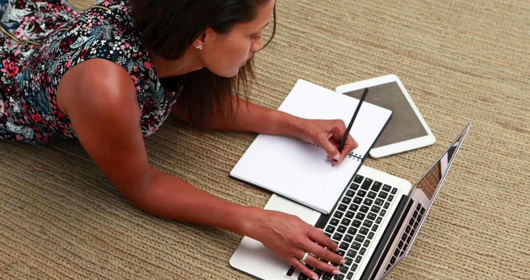 Woman Working on Laptop Taking Notes in Notebook on Beige Carpet - Free Images, Stock Photos and Pictures on Pikwizard.com