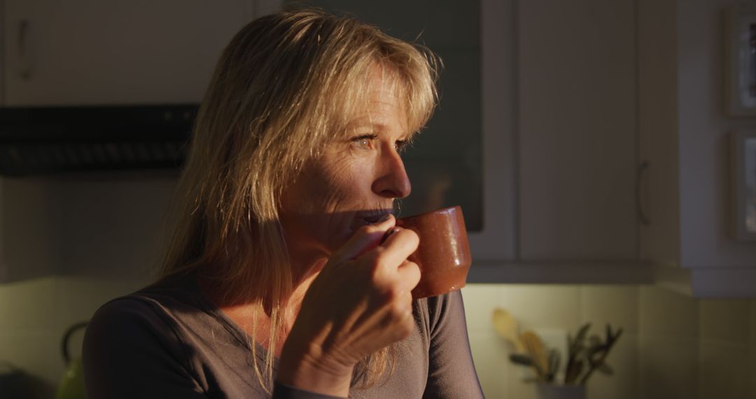 Pensive Middle-aged Woman Drinking Coffee in Kitchen During Sunset - Free Images, Stock Photos and Pictures on Pikwizard.com