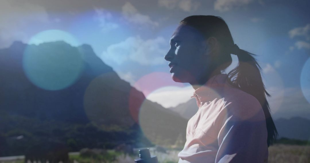 Backlit woman watching mountain peaks with binoculars, silhouette and lens flare bokeh