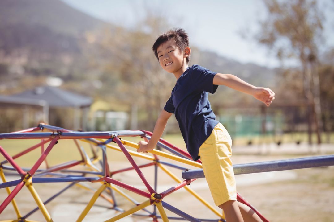 Asian Boy Balancing on Colorful Climbing Dome in Sunny Playground