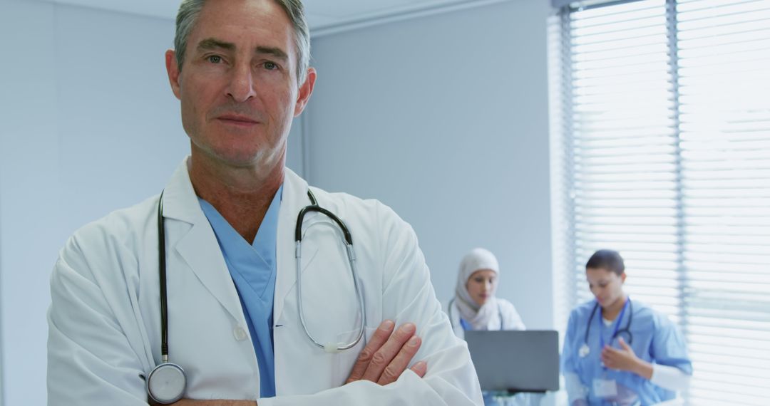 Experienced Doctor Standing with Stethoscope, Nurses Working in Background - Free Images, Stock Photos and Pictures on Pikwizard.com