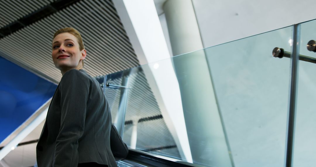 Smiling Businesswoman Riding Escalator in Modern Office Building - Free Images, Stock Photos and Pictures on Pikwizard.com