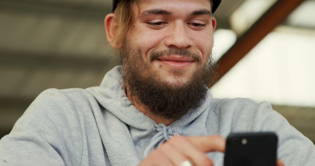 Young hipster man using smartphone smiling in casual setting - Free Images, Stock Photos and Pictures on Pikwizard.com