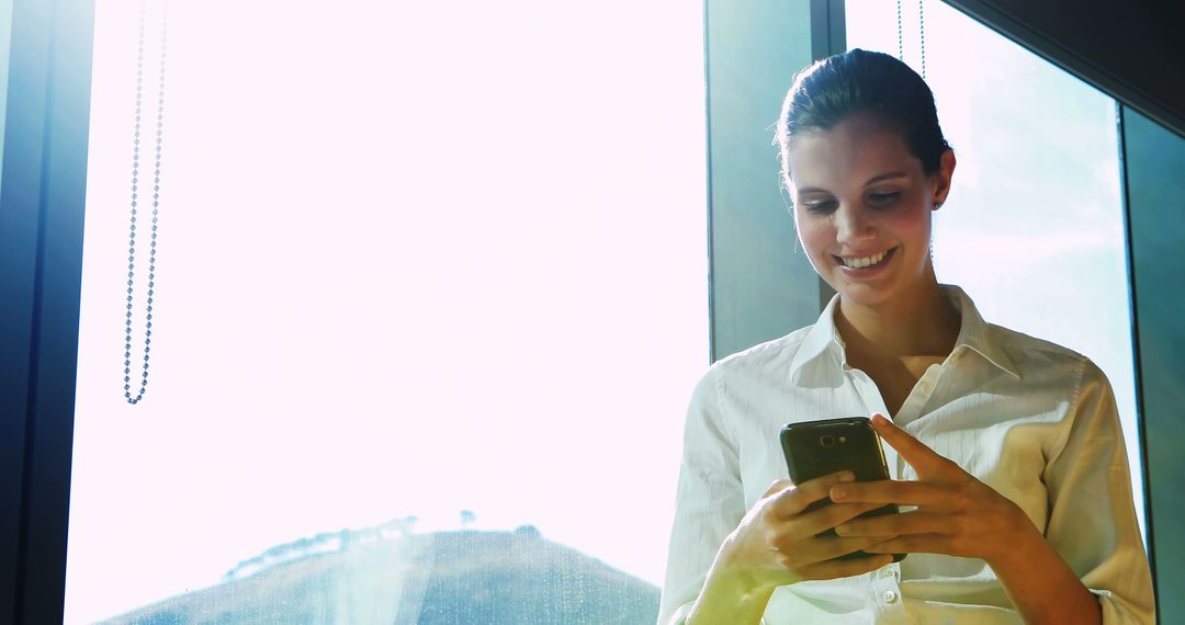 Young Businesswoman Using Smartphone by Large Window - Free Images, Stock Photos and Pictures on Pikwizard.com