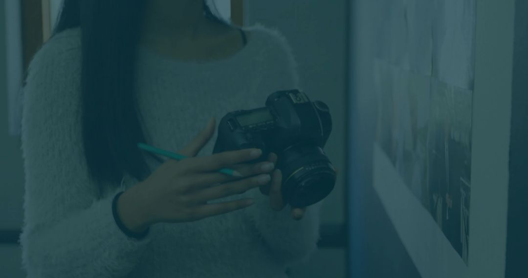 Young photographer inspecting mounted print holding DSLR camera and pen in classroom studio
