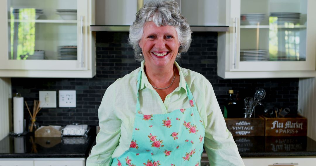 Smiling Senior Woman in Kitchen Wearing Floral Apron - Free Images, Stock Photos and Pictures on Pikwizard.com