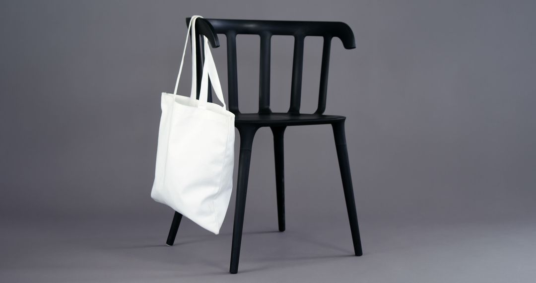 A white tote bag hangs on a sleek black chair against a neutral background, with copy space - Free Images, Stock Photos and Pictures on Pikwizard.com