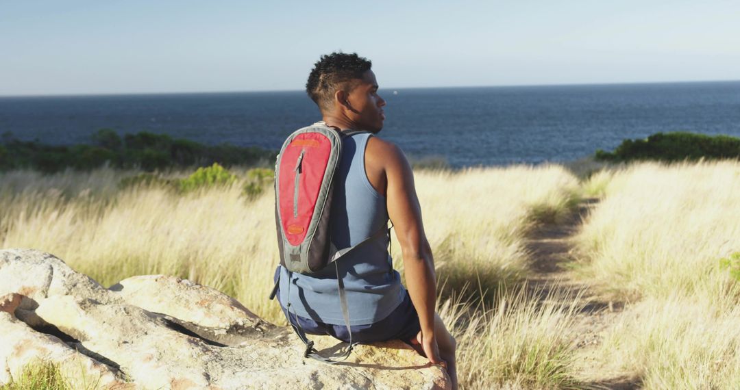 Man Relaxing on Coastal Dunes with Hydration Backpack Overlooking Ocean