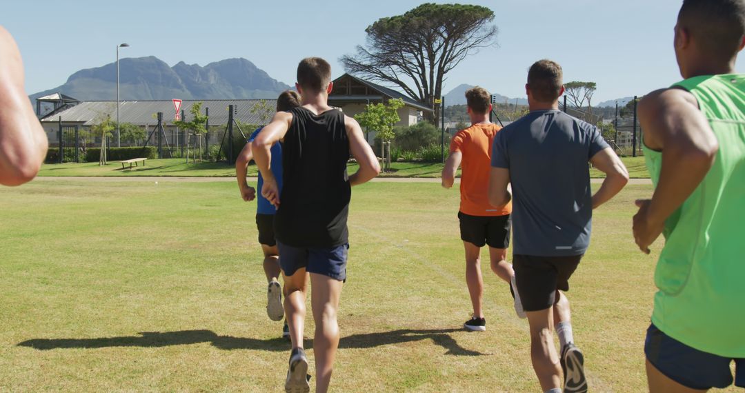 Group of Young Athletes Running on Grass Field with Mountains in Background - Free Images, Stock Photos and Pictures on Pikwizard.com