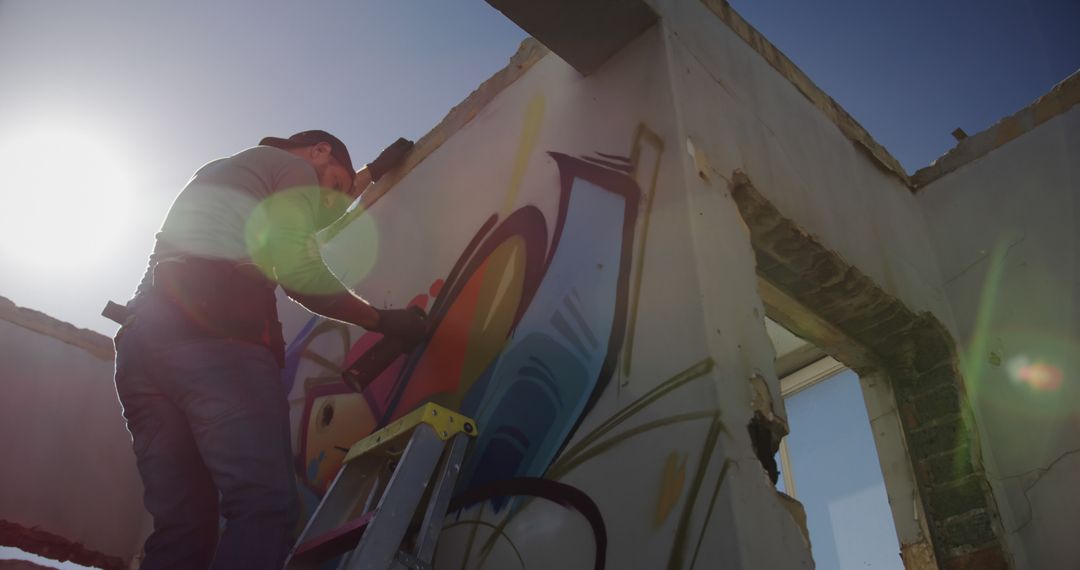 Graffiti Artist Painting Mural on Urban Building in Sunlight - Free Images, Stock Photos and Pictures on Pikwizard.com