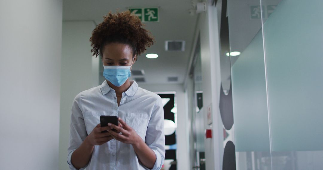 Young Woman Wearing Face Mask Using Smartphone in Office Corridor - Free Images, Stock Photos and Pictures on Pikwizard.com