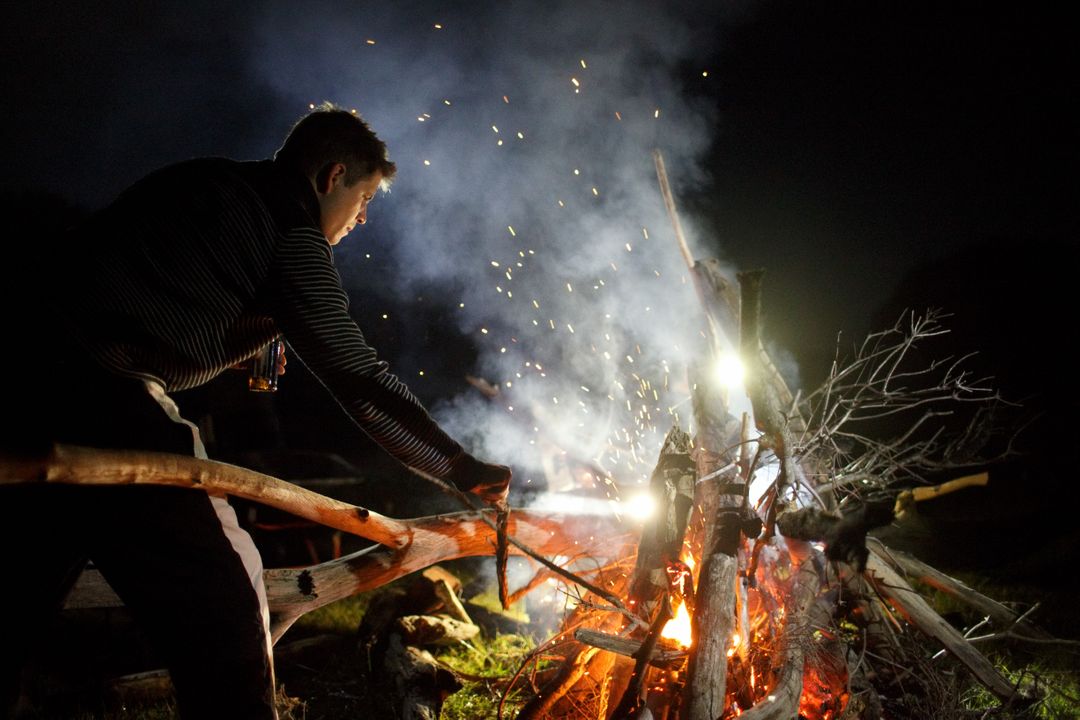 Man Standing by Campfire at Night, Stoking Flames with Stick - Free Images, Stock Photos and Pictures on Pikwizard.com