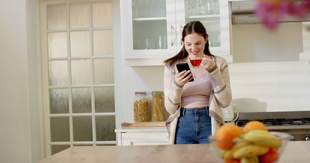 Young Woman Enjoying Morning Coffee and Browsing Smartphone in Modern Kitchen - Free Images, Stock Photos and Pictures on Pikwizard.com