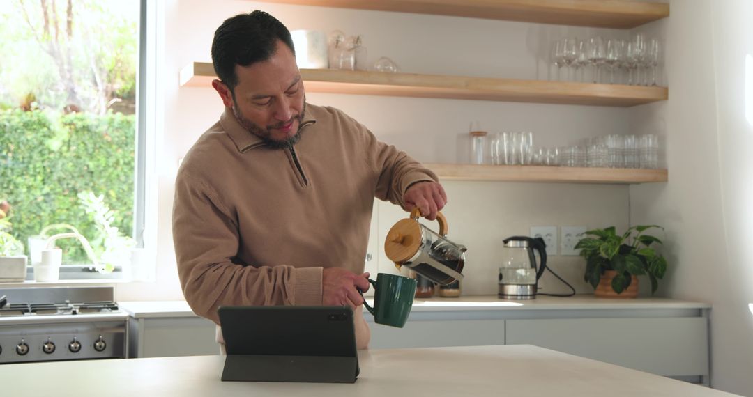 Man Using Tablet While Pouring Coffee from French Press in Modern Kitchen