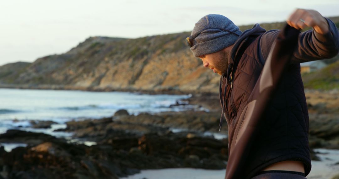 Male Surfer Prepares Wetsuit on Rugged Beachside - Free Images, Stock Photos and Pictures on Pikwizard.com