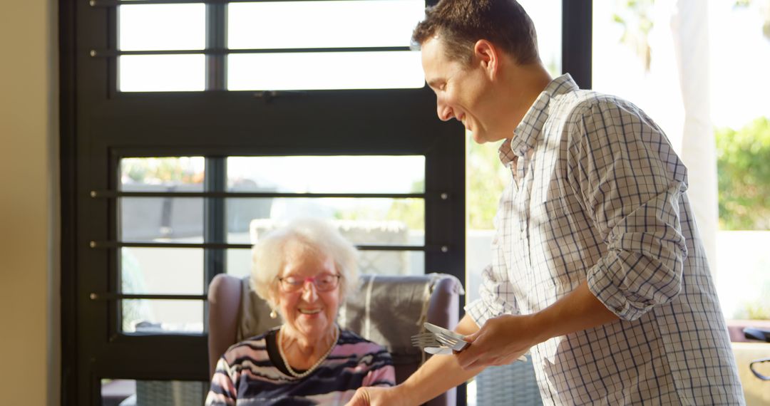 Smiling Young Man Serving Meal to Elderly Woman in Bright Home - Free Images, Stock Photos and Pictures on Pikwizard.com