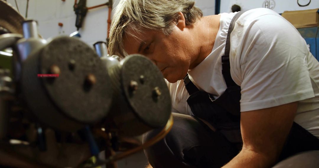 Experienced mechanic adjusting industrial rollers and shafts in busy metalworking workshop