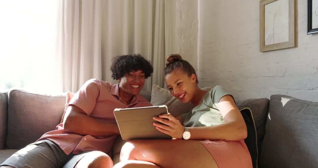 Couple Relaxing On Sofa Using Tablet In Sunlit Living Room