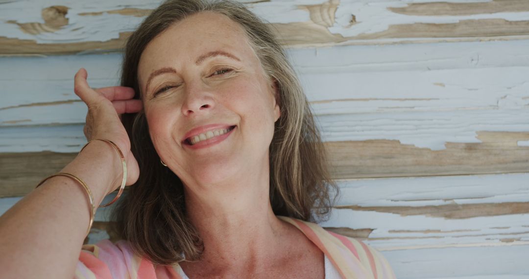 Smiling Middle-Aged Woman Relaxing by Weathered Wooden Wall - Free Images, Stock Photos and Pictures on Pikwizard.com