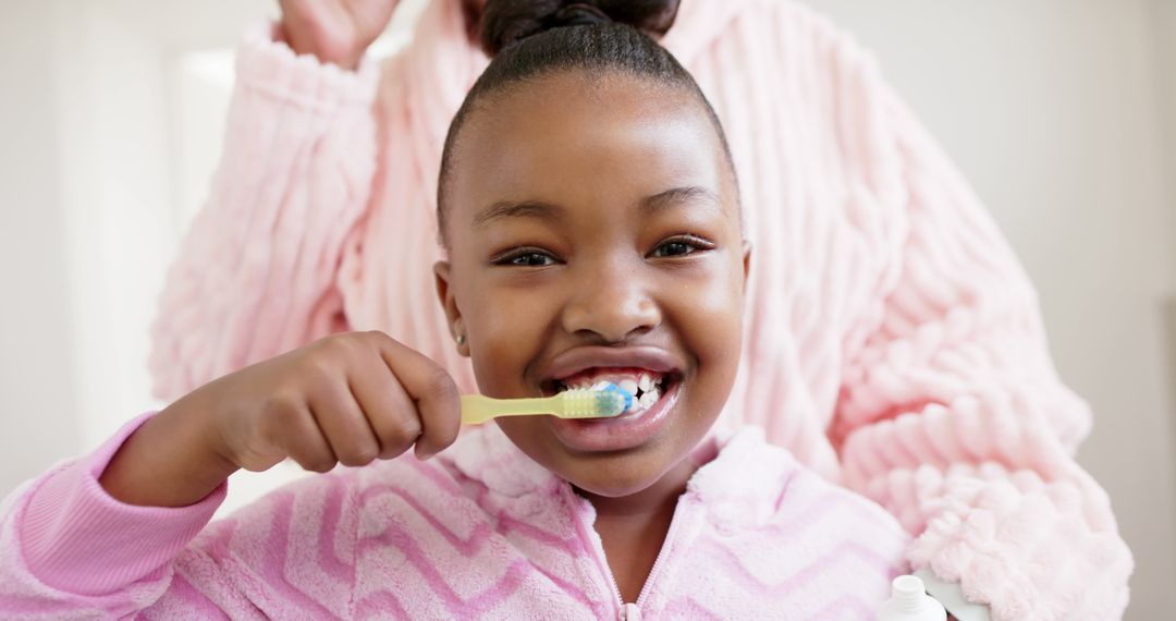 Smiling Young Girl Brushing Teeth with Supportive Parent Nearby - Free Images, Stock Photos and Pictures on Pikwizard.com