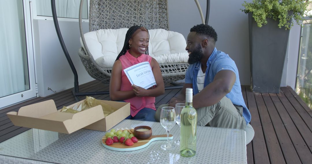 Couple Joyfully Unboxing Gift on Patio with Wine and Fruit