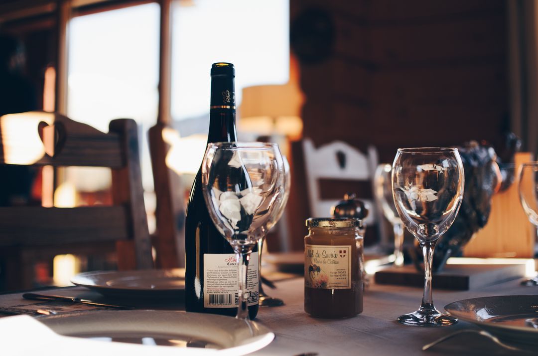 Rustic cozy dinner table featuring red wine bottle, crystal wine glasses and artisanal jam