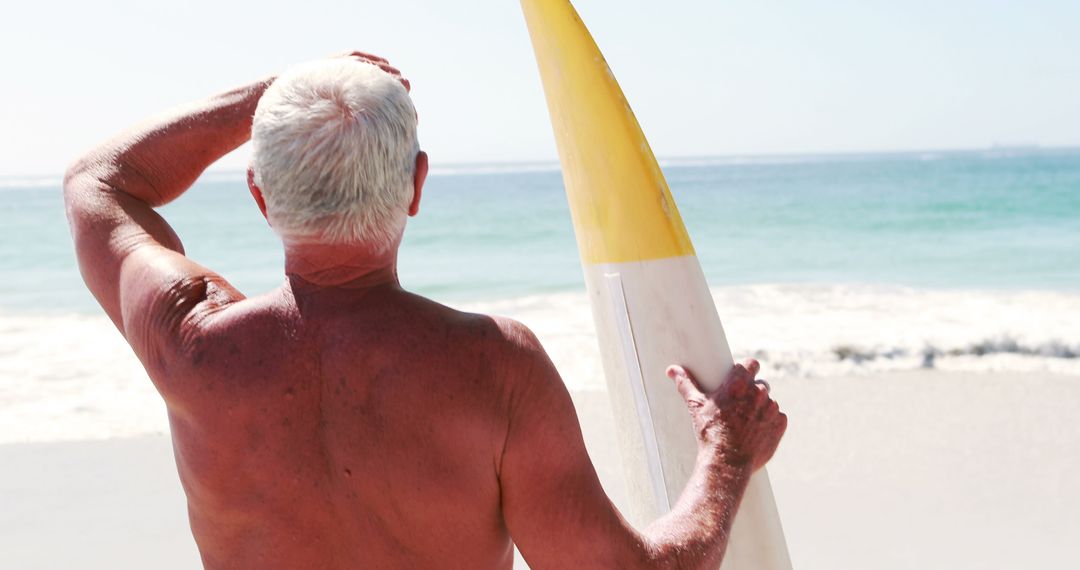 An elderly man pauses with his surfboard on the beach, poised for a surf. - Free Images, Stock Photos and Pictures on Pikwizard.com