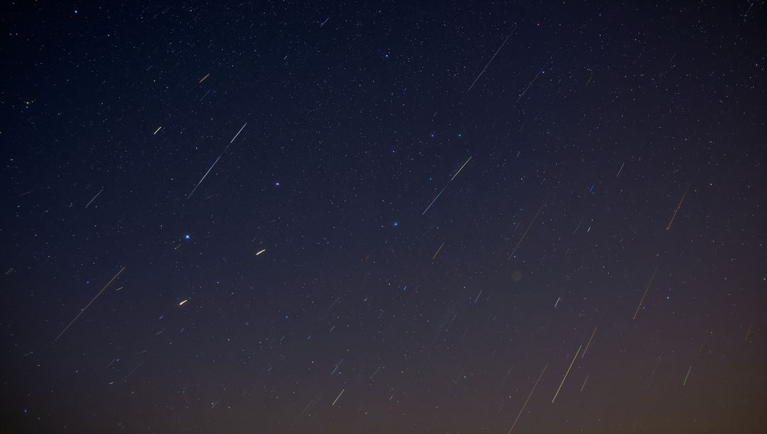 Meteor Shower Streaking Across Starfield Over Rural Horizon With Faint Orange Glow