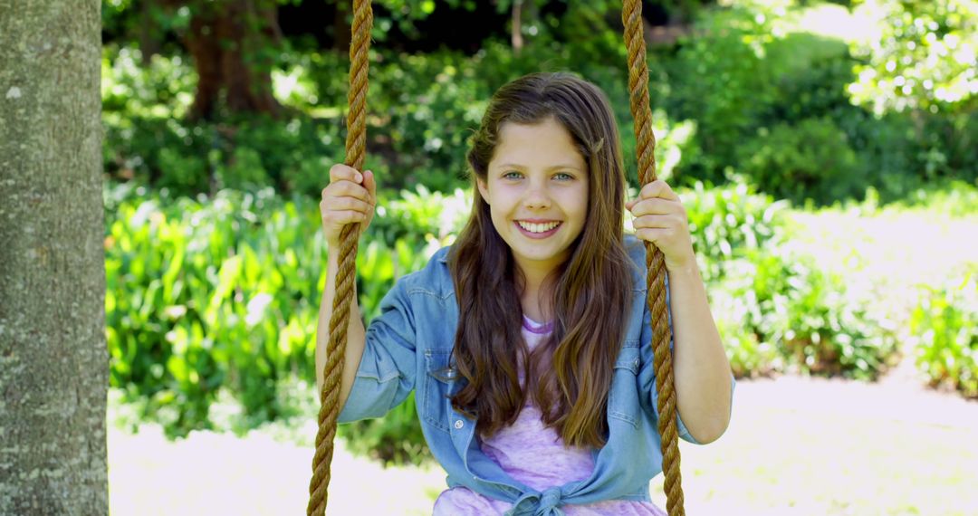 Smiling girl sitting on rope swing in sunny garden - Free Images, Stock Photos and Pictures on Pikwizard.com