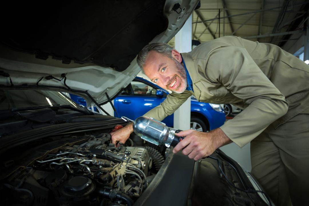 Mechanic Smiling While Examining Car Engine in Repair Garage - Free Images, Stock Photos and Pictures on Pikwizard.com