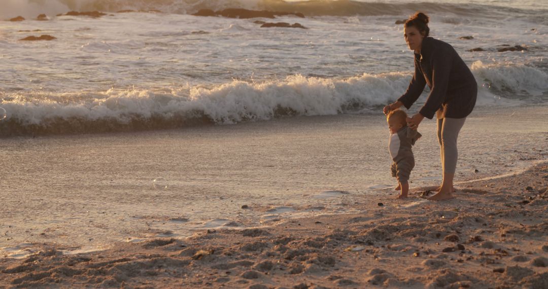 Mother Helping Toddler to Walk Along the Seashore at Sunset - Free Images, Stock Photos and Pictures on Pikwizard.com