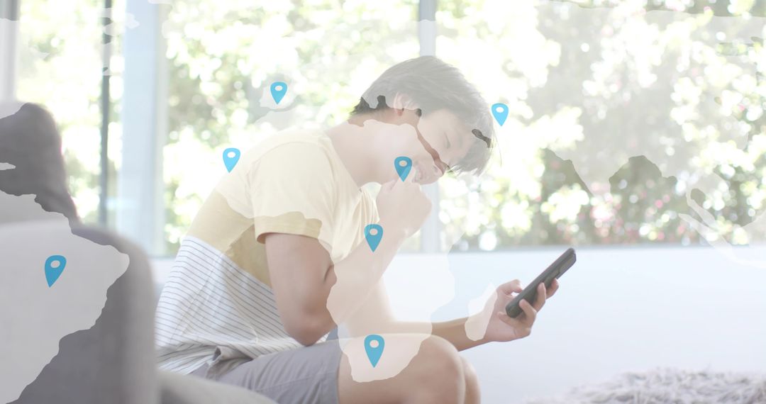 Young Asian man sitting and using smartphone in bright home with global map pins overlay